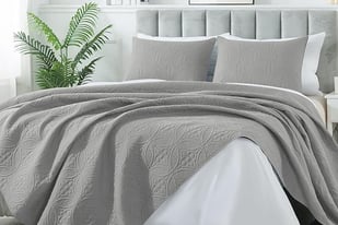 a bed with a grey bedspread and a plant
