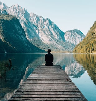 una persona seduta su un molo con il lago e le montagne davanti
