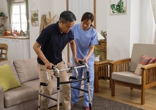 home physiotherapist helping a neurological patient walk using a walker for balance.