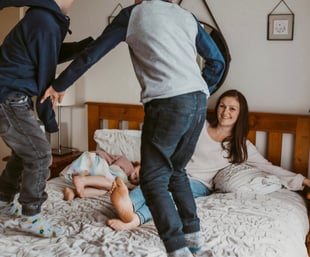 two young boys jumping on a bed with their mother