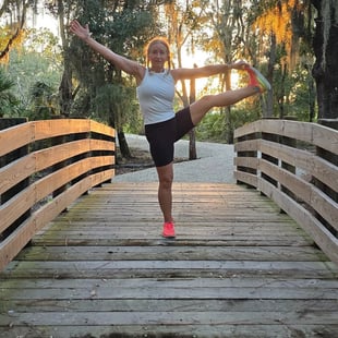 Eva practicing balance yoga pose on a wooden bridge at sunset, surrounded by nature.
