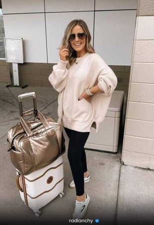 a woman in a white sweater and black leggings and a suitcase