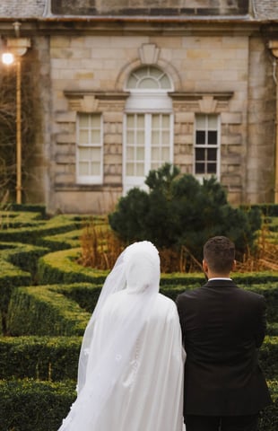 a bride and groom in formal attire standing in front of a castle