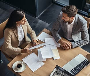 Two business people sitting at a table with papers and laptops