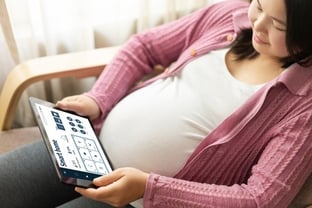 pregnant east asian woman looking at smart home tablet