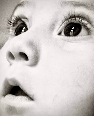 Black and white close-up of a baby girl's face, looking upward with wide eyes, capturing a sense of wonder and innocence