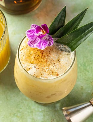 overhead shot of a beachy orange cocktail with flowery island garnishes