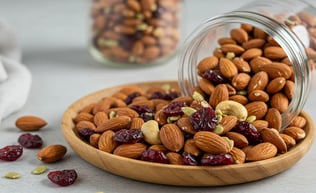 A plate of almonds, cashews, dried cranberries, and pumpkin seeds with a spilled jar in the background.