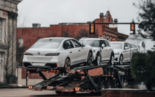 Cegonha ou carreta de transporte de veículos, trafegando por um bairro estilo antigo.