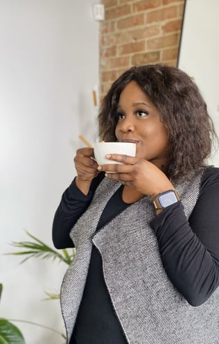 a black plus size woman nutritionist in a vest and jeans is holding a cup of coffee