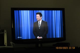 Jimmy Fallon standing in front of a blue curtain 