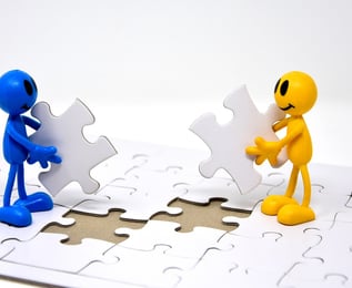 Two cartoon figures connecting puzzle pieces, symbolizing collaboration and integration
