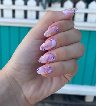 hand in loose fist showing manicure with different shades of purple and floral abstract design