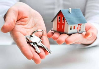 Manos sosteniendo una maqueta de casa junto a una llave, representando seguridad en la gestión