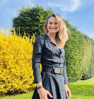 Caroline stood outside on a sunny day by hedgerows she is smiling.