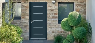 Porte d'entrée en aluminium noir sur une maison à façade en pierre