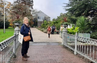 O femeie într-o haină albastră, într-o grădină plină cu flori.