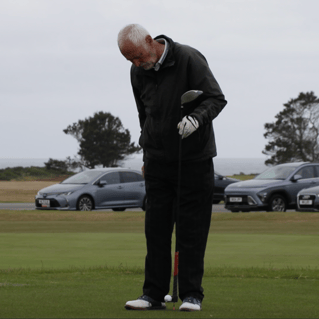 A golfer standing with a driver in hand, preparing for a shot using the TeeZUP tool to position the golf ball on a tee.