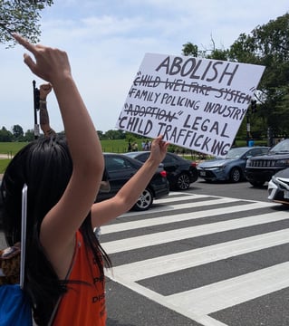 Woman holding sign that says, "Abolish family policing industry and legal child trafficking."