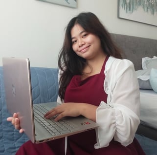 Smiling woman in a red dress and white cardigan using a silver HP laptop on a couch.