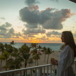 girld in a balcony in Lago Mar Beach Resort & Club with a sunrise and beach in the background 