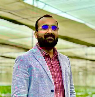 a man in a suit and sunglasses standing in a greenhouse