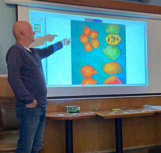 Man standing in front of a slide showing pawpaws and other fruit for size comparison