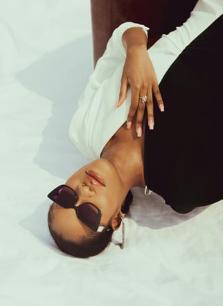 a woman in a white shirt and sunglasses laying on a bed