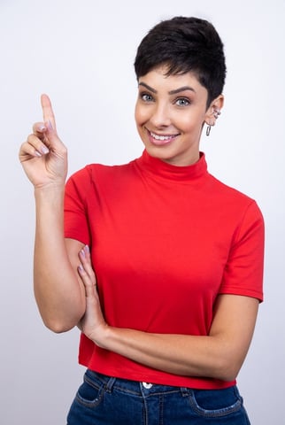 mulher de cabelo curto olhos azuis sorrindo apontando para cima, com blusa vermelha em fundo branco