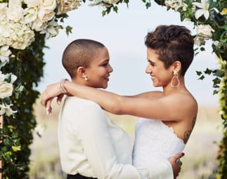 a lesbian couple at their wedding celebration under the arbour / bower dress in white 