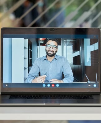 A laptop screen showing a video call with a man in a business shirt holding a pen
