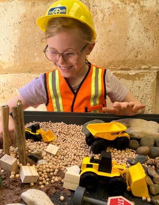 Smiling child in a construction outfit playing with a sensory construction site small world play.