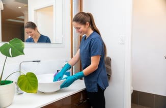 a woman in a blue shirt and gloves cleaning a sink