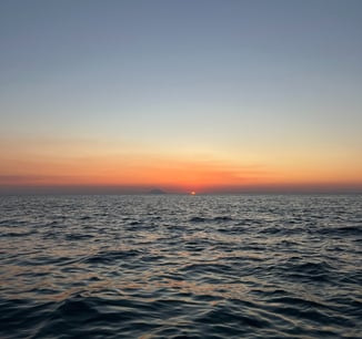 a sunset over the ocean with a boat in the distance