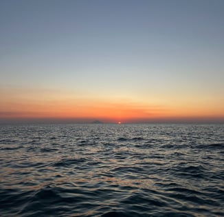 a sunset over the ocean with a boat in the distance