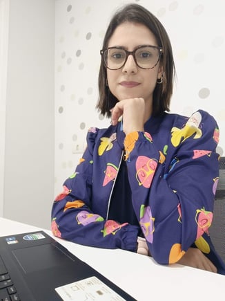 a woman in glasses and a blue jacket sitting at a desk
