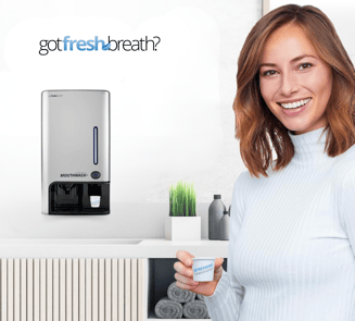 Mujer usando el dispensador de enjuague bucal GotFreshBreath montado en pared, ideal para espacios p