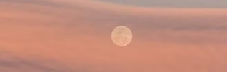 a full moon in the sky with a pink sky