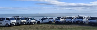 A group of JB Painting & Plastering vans parked in a row in front of the sea.