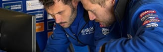 two men in blue jackets looking at data on a laptop