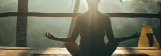 Person meditating in lotus position during sunrise at a tropical wellness retreat