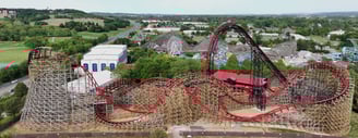 A black and red wooden roller coaster with several rides in the background