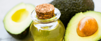 Une bouteille en verre avec l'huile d'avocat dedans et des avocats en fond