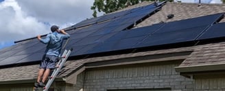 A man standing from a ladder cleaning solar panels on a roof with a water pool