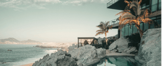 Modern cliffside villa with ocean view, palm trees, and infinity pool at sunset