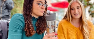 Two Girls talking and one is sipping a bottle of tea