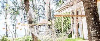 **Alt-Text:**  A white rope hammock hanging between two palm trees in a tropical garden on Koh Samui