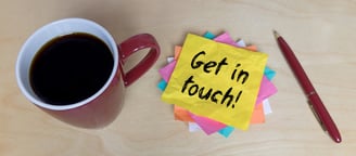 a cup of coffee, pen on a desk and a pile of coloured post-it notes. Top one says Get In Touch