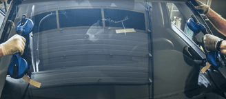 two workers hold windshield with suction cups