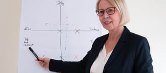 a woman in a business suit is holding a pen and pointing at a white board